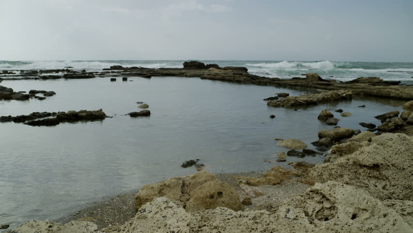 Panoramic right to left of waves rolling over  remaining partial ruin and pool