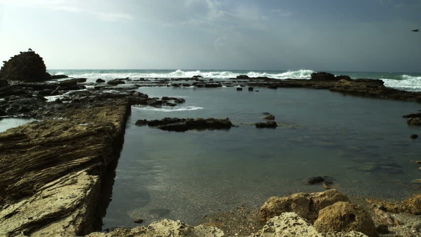 Panoramic left to right of waves rolling over  remaining partial ruin and pool