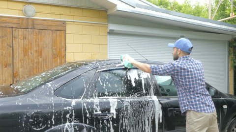 Man washing his black car near the house.