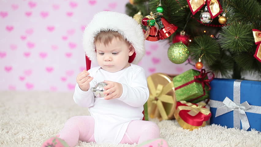 Newborn in santa hat beside a Christmas tree 