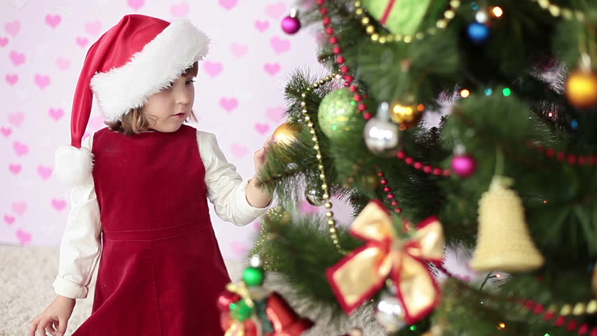 Girl in santa cap dresses up Christmas tree