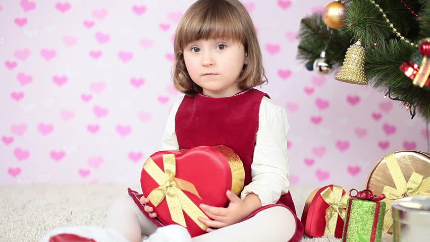 Laughing girl on the floor near a Christmas tree with gift in hand