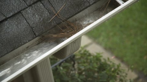 Heavy rain running off a house roof to a clogged gutter