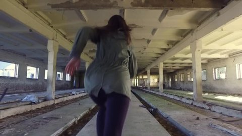 The girl run away from killer in abandoned building through the hallway. Back view horror dark mood. Steadicam shot. Smooth tracking. Old abandoned place. Slow motion.