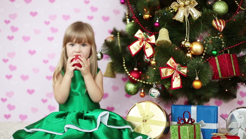 Girl eating an apple near a Christmas tree. She sits on the floor