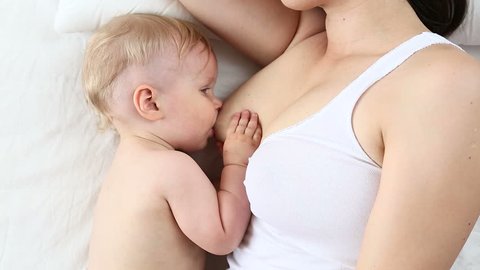 Happy young mother breastfeeding her baby lying on the bed. Top view of Mom breast feeding her son