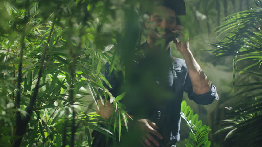 Adventurer in Hat using Talking on Mobile Phone in Jungle Forest.