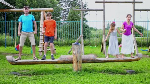 Children and parents swing on playground at summer day