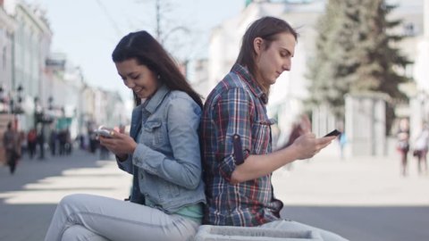 Cute girl and boy with long hair use gadgets on a street in dating time-lapse