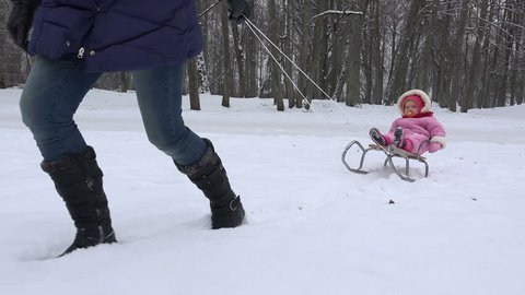 mother pull sledge with baby daughter on snow in winter nature. Handheld. 4K