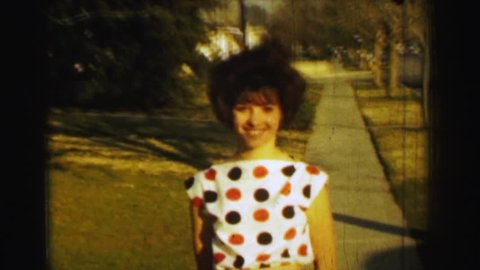 ST. LOUIS, MISSOURI 1958: Teenage girl curly perm hair polka dot blouse small orange shorts.