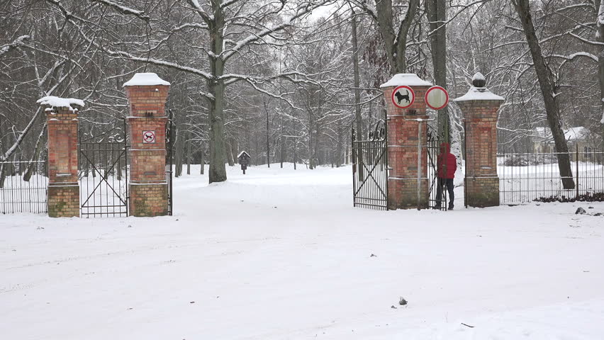 Man with warm clothes enter snowy winter park gate entrance and snow fall. 4K