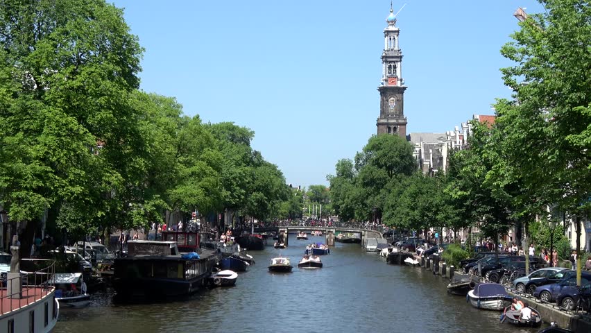 Amsterdam city center showing Westertoren church Westerkerk and typical Amsterdam canal Prinsengracht busy because of summer day blue sky background small boats moving over gracht tourist visit 4k