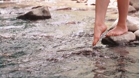Slow motion video of a bare feet woman splashing and kicking her legs in the water in a river with a slow stream