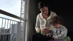 Mother and child (age 30 and 2) play on mobile phone together at home.