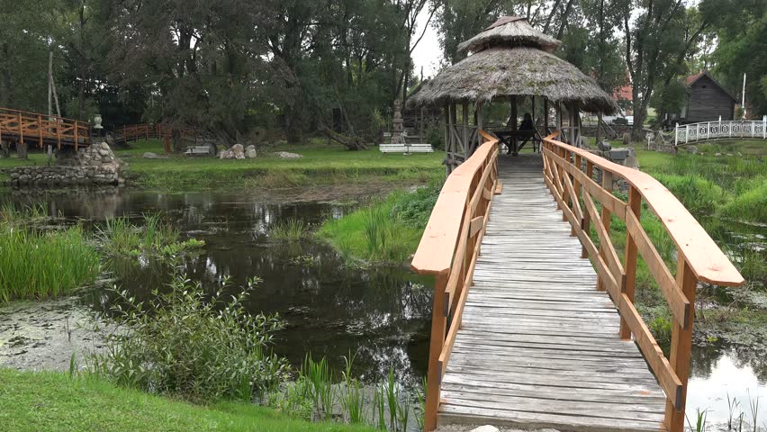 young happy smiling nice woman walk on vintage rural wooden bridge over small stream. 4K UHD video clip.