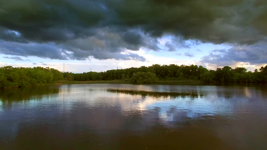 Wooded marshland under dark sky, gliding over calm the waters, gliding low, aerial view.