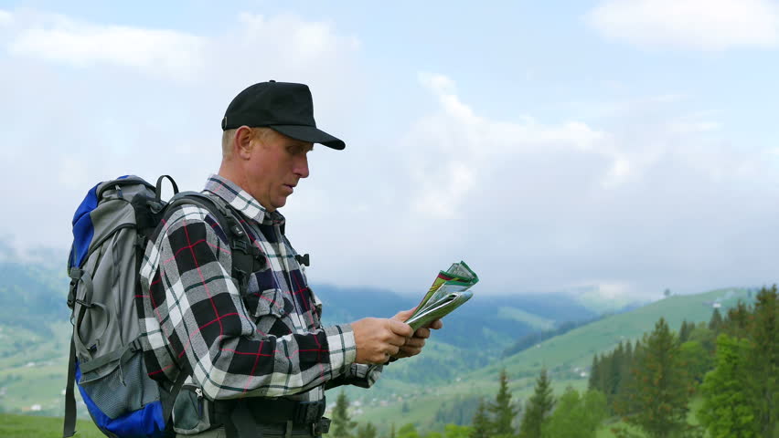 4K . Tourist backpacker team. Adult man on mountains looks for  way through paper map