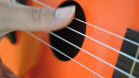 person playing orange ukulele on neutral background