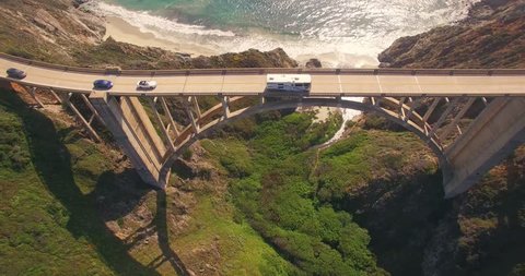 Aerial view RV, cars passing Bixby Creek Bridge on PCH Highway 1 with Pacific Ocean in background. Monterey, Big Sur, CA