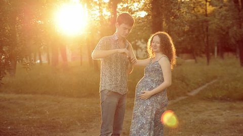 Loving couple, a pregnant girl with the guy standing on the lawn in the Park at sunset, play and blow bubbles.