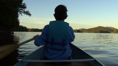 Boy canoes across lake (POV of person behind)
