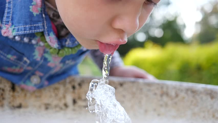 Cute little girl face portrait drink water in a park from drinking fountain slow