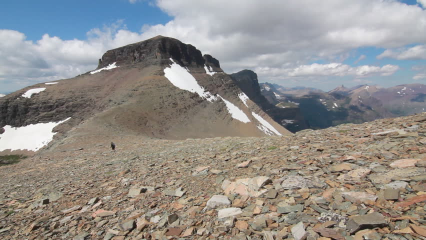 Girl hiking in the distance over the saddle of a rocky mountain towards the
