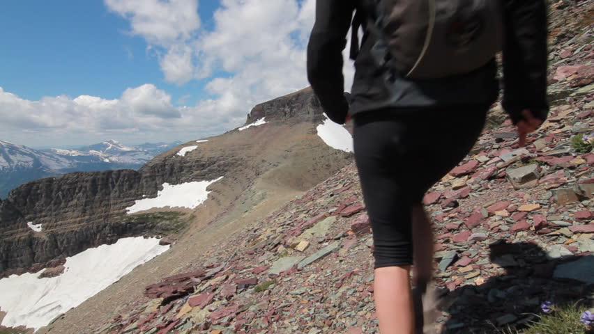 Girl hiking in the distance over the saddle of a rocky mountain towards the