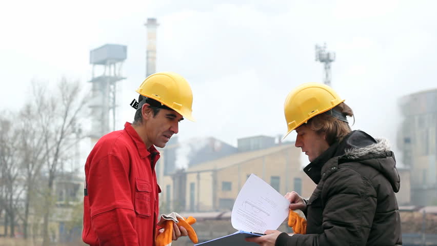 Two Co-Workers Discussing a Document. Supervisor in yellow hardhat , talking to factory worker outside the industrial facility. HD 1080i. Canon EOS 550D.