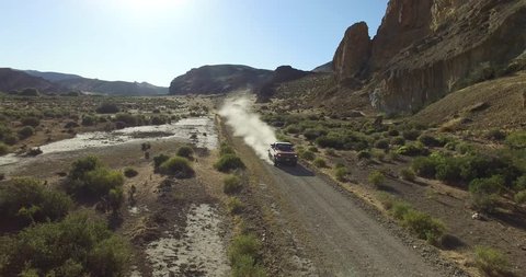 Aerial scene of car traveling on dirt road a dry, rocky, landscape. Monumental scenery. Car leves dust while driving. Fast scene. Canyon of Piedra Parada, Chubut, Patagonia Argentina. Hiking place. 
