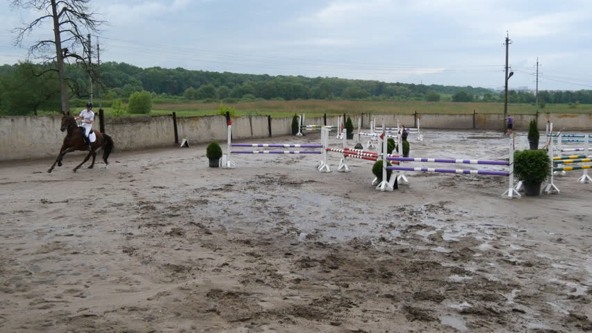 Professional female jockey rides on horseback. Horse runs on the sand and jumps through a barrier.