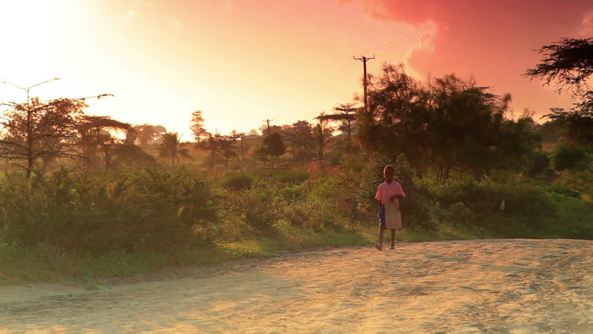 KENYA, AFRICA - CIRCA 2011: Small boy walks along dirt road at sunrise in Africa