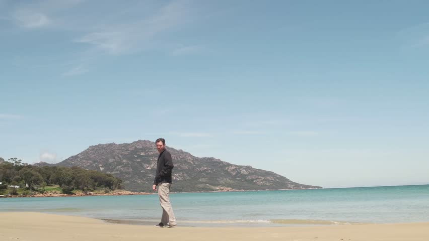 man smiling and walking along beach Tasmania