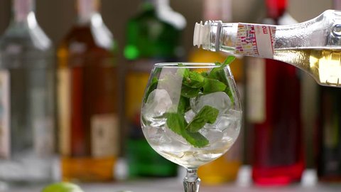 Bottle pours drink into glass. Mint leaves inside a wineglass. Sweet elderflower syrup. Key ingredient for hugo cocktail.