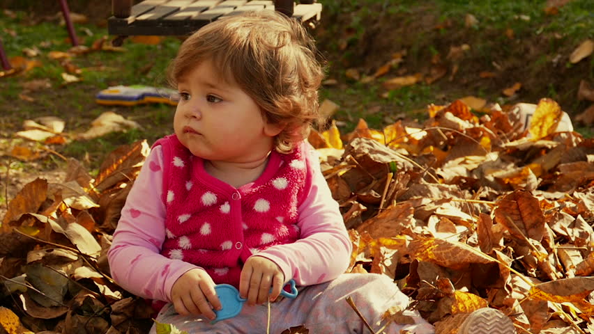 Baby girl sitting on dry autumn leaves and starting to giggle and dance