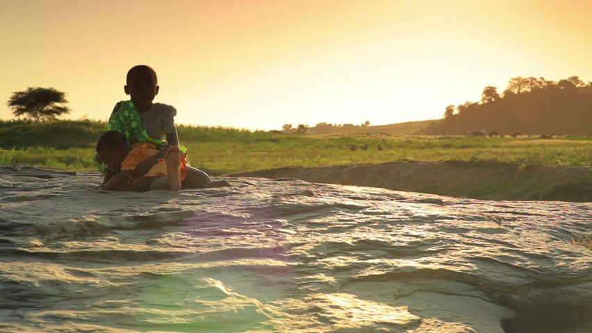 KENYA, AFRICA - CIRCA 2011: Girl sits on rock with baby at sunset.