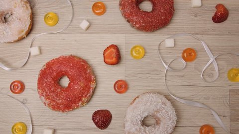 Donuts, sweetmeats candy and strawberry on wooden background. Background of coconut and berry homemade glazed and filled donuts. Assorted colorful red and white sweet sugar donuts and sweets. : vidéo de stock