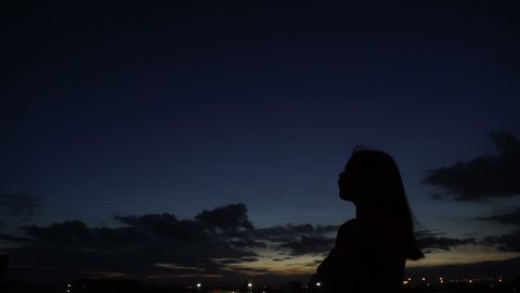 Silhouette of woman looking up at sunset sky with wind blowing hair
