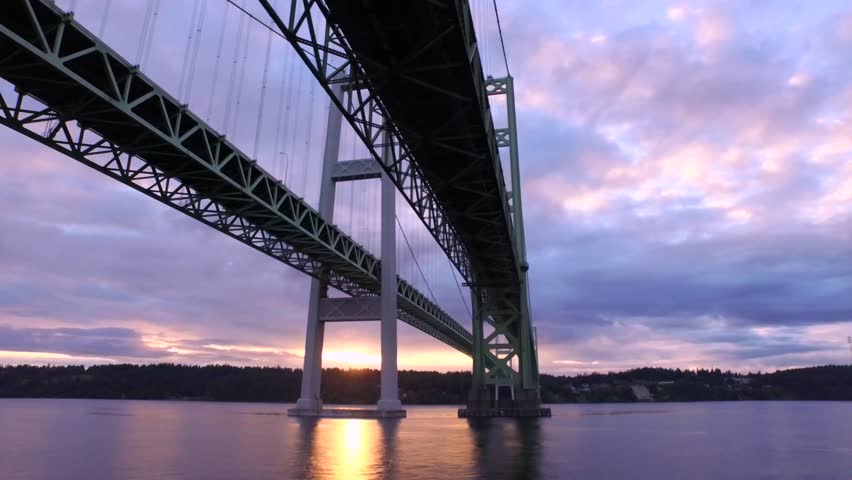 Aerial flight under the Narrows Bridge in 4k. Busy car traffic travels over the suspension bridge of the Puget Sound in Washington state