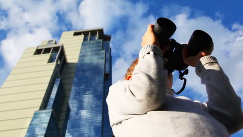 inquisitive boy looks through binoculars and turns on background of skyscrapers