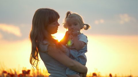 Mother hugs lovely child daughter in poppies field with sunset sunlight and flare effect