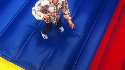 Young girl (female age 6) jumping on bouncing castle and screaming from joy looking up at the camera. Full length body.Real people. Copy space