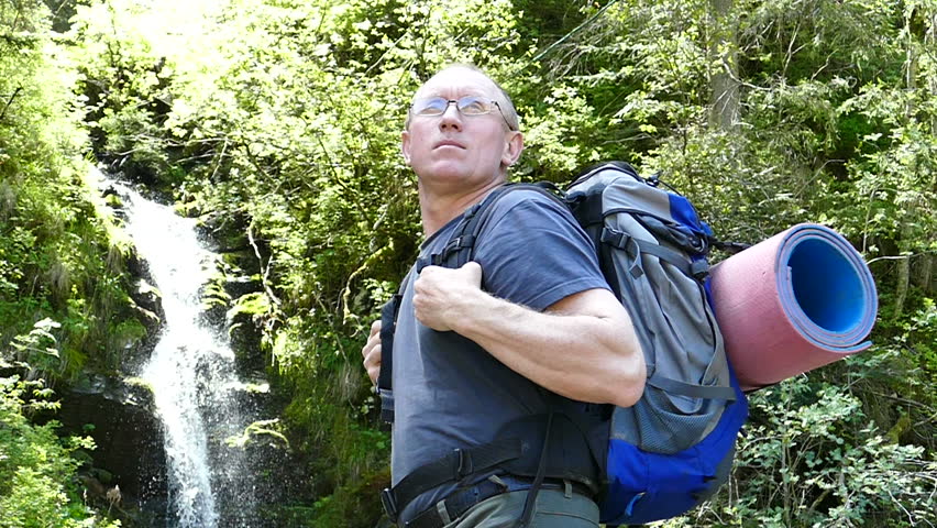 Slow motion. Man tourist stand backpacker near waterfall. Focus change