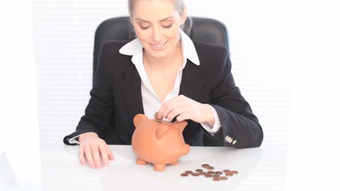 Business Piggy Bank Savings, a smiling businesswoman sits at her desk placing coins in a piggy bank, savings concept