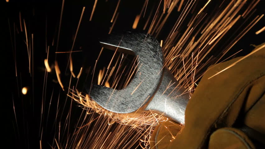 Sparks fly past a wrench held in a workers' hand