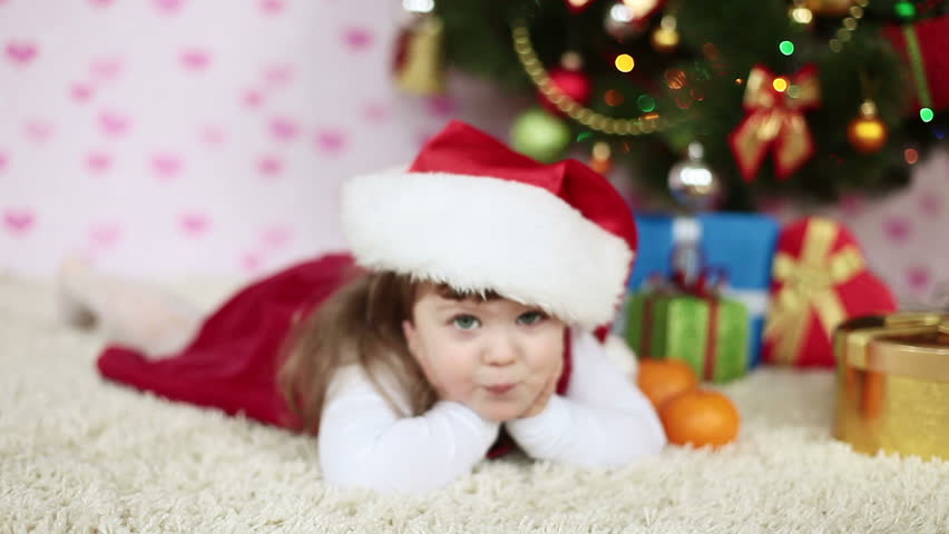 Baby girl in a Santa hat lying on the carpet. Slow motion