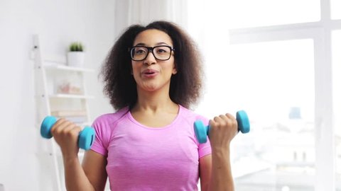 fitness, sport, training and people concept - happy african woman exercising with dumbbells at home