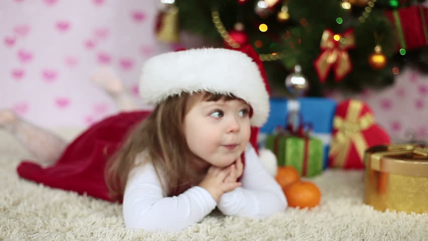 Baby girl in a Santa hat lying on the floor. Looking at camera. Slow motion