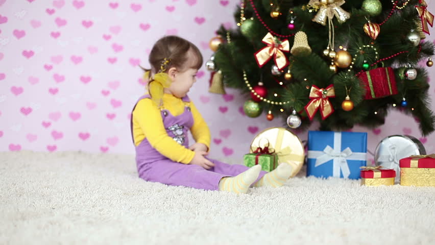 Baby girl is sitting on the floor near the Christmas tree